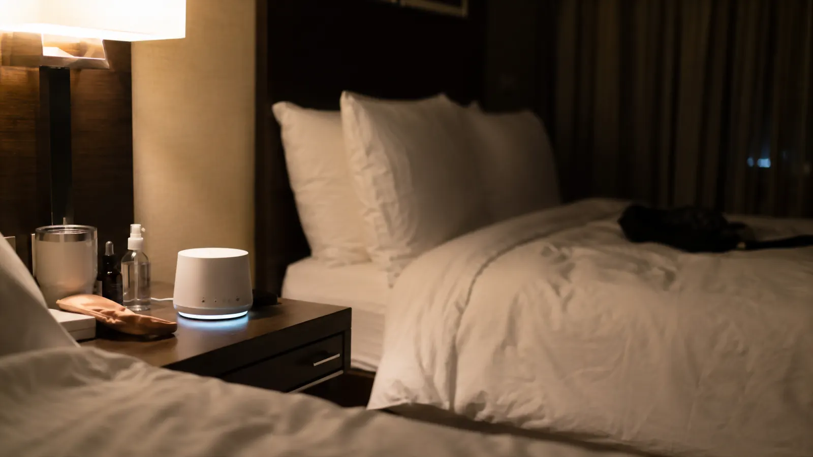 Dreamegg white noise machine sitting on a cluttered shared hotel nightstand at night