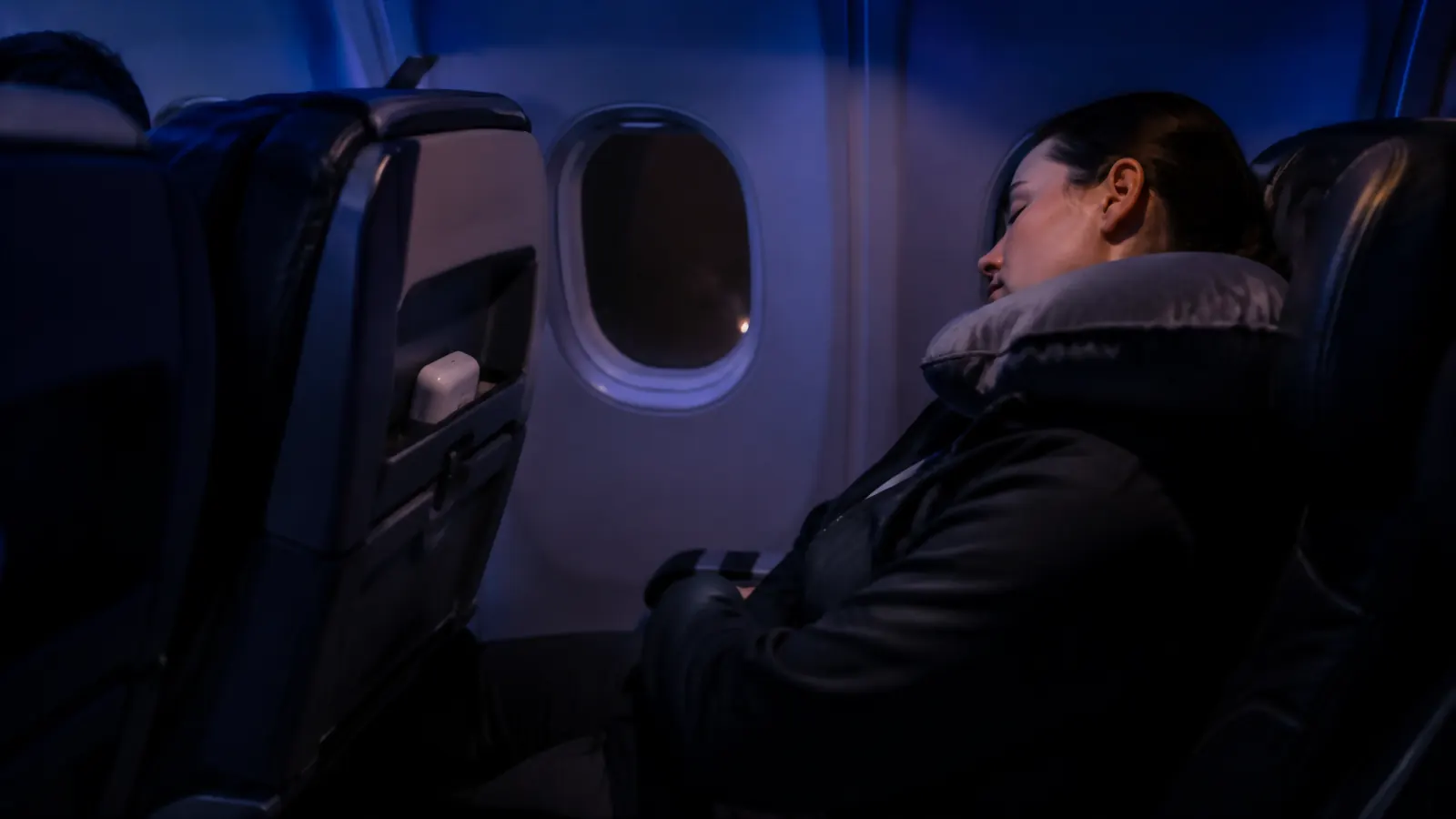 Dim airplane cabin at night with a small white sound machine tucked into a seatback pocket