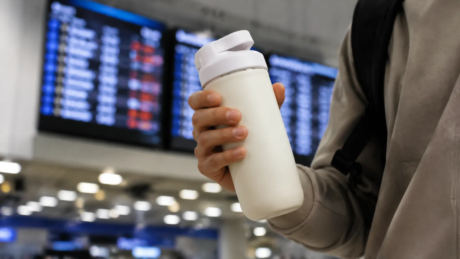 Close-up of a hand holding the Owala SmoothSip tumbler with a departures board blurred in the background