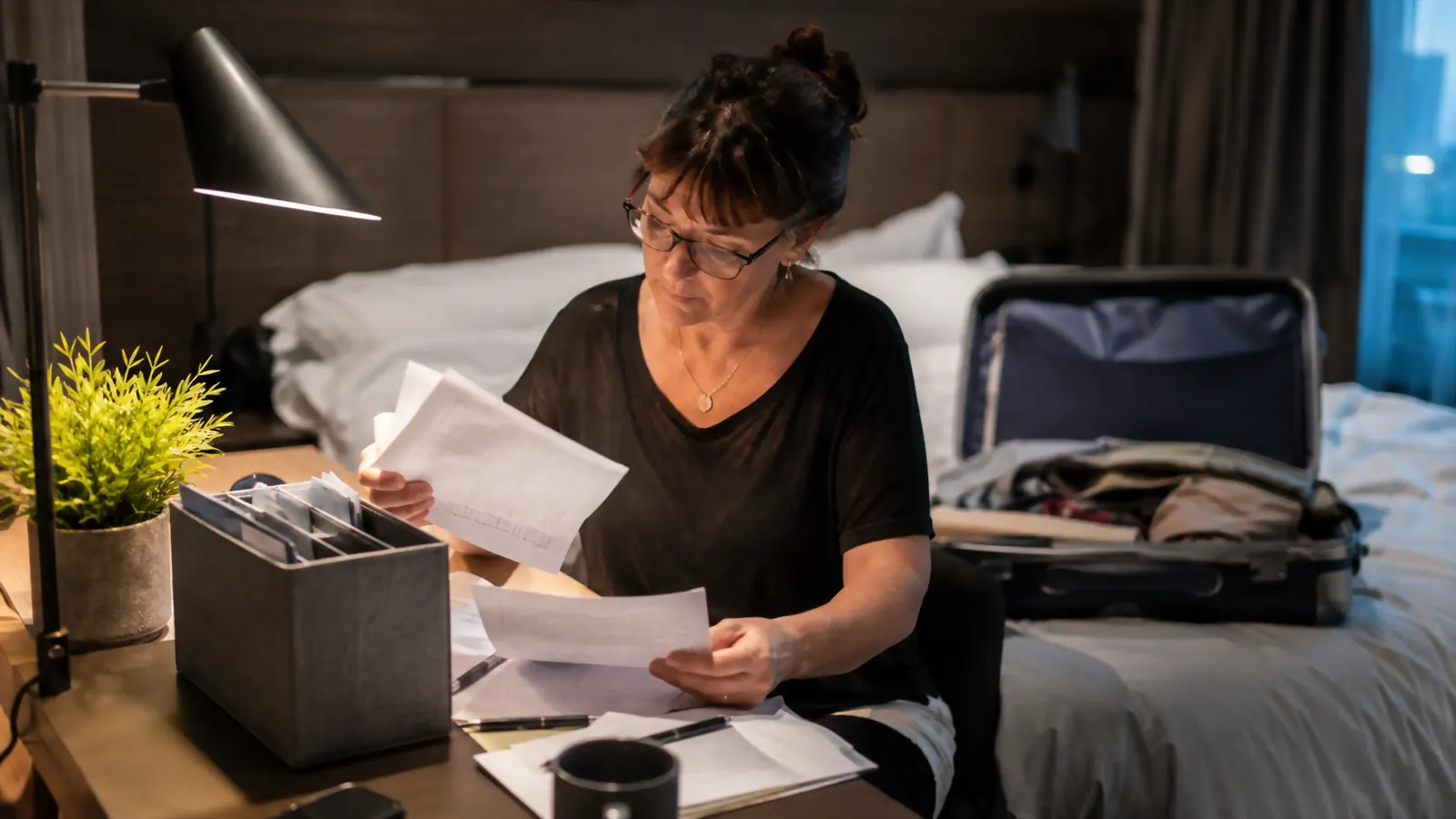Parent double checking a stack of documents against a printed itinerary at a hotel desk